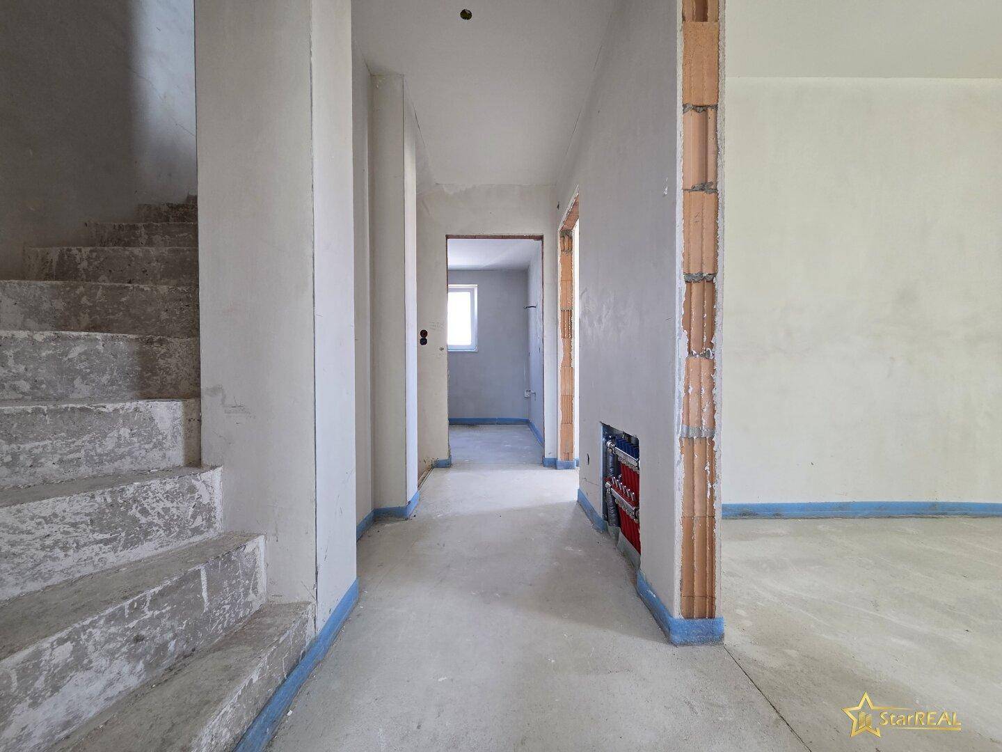 Flur im Rohbau mit Treppenaufgang und sichtbaren Mauerwerkdetails, bereit für den Ausbau.