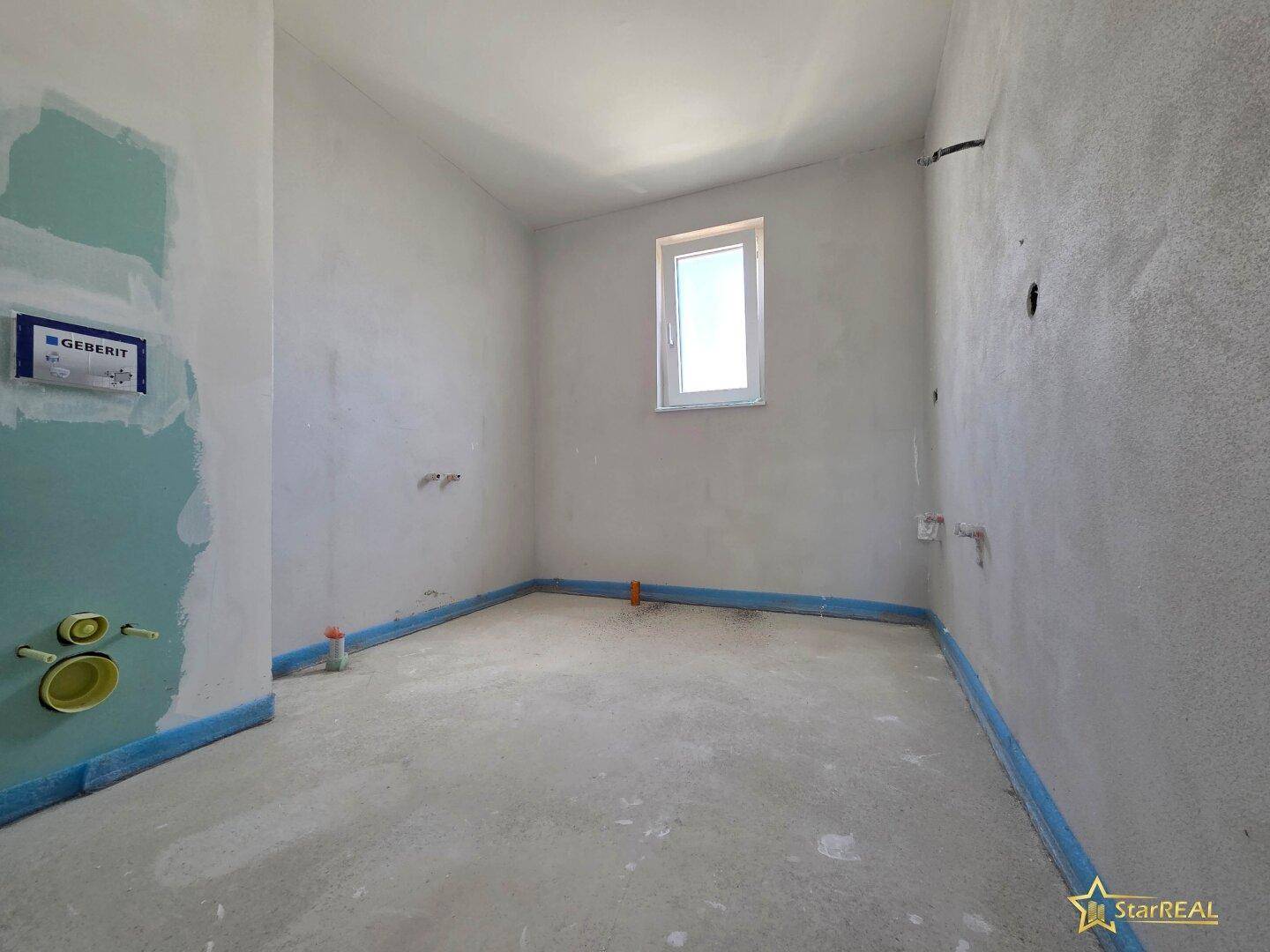 Badezimmer im Rohbau mit Fenster und vorbereiteten Anschlüssen für Sanitärinstallationen.