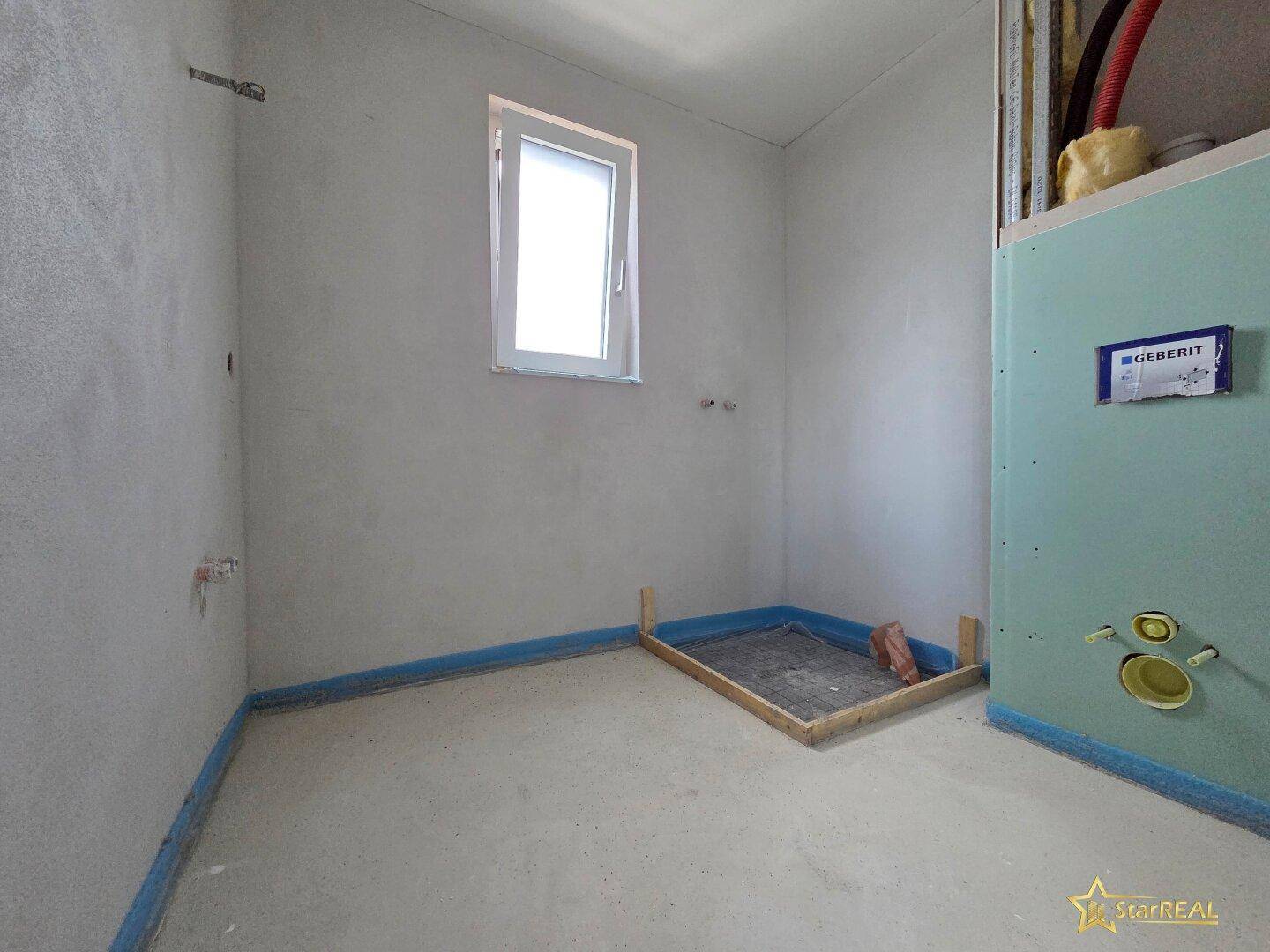 Badezimmer im Rohbau mit Fenster und vorbereiteten Installationen für Dusche und WC.