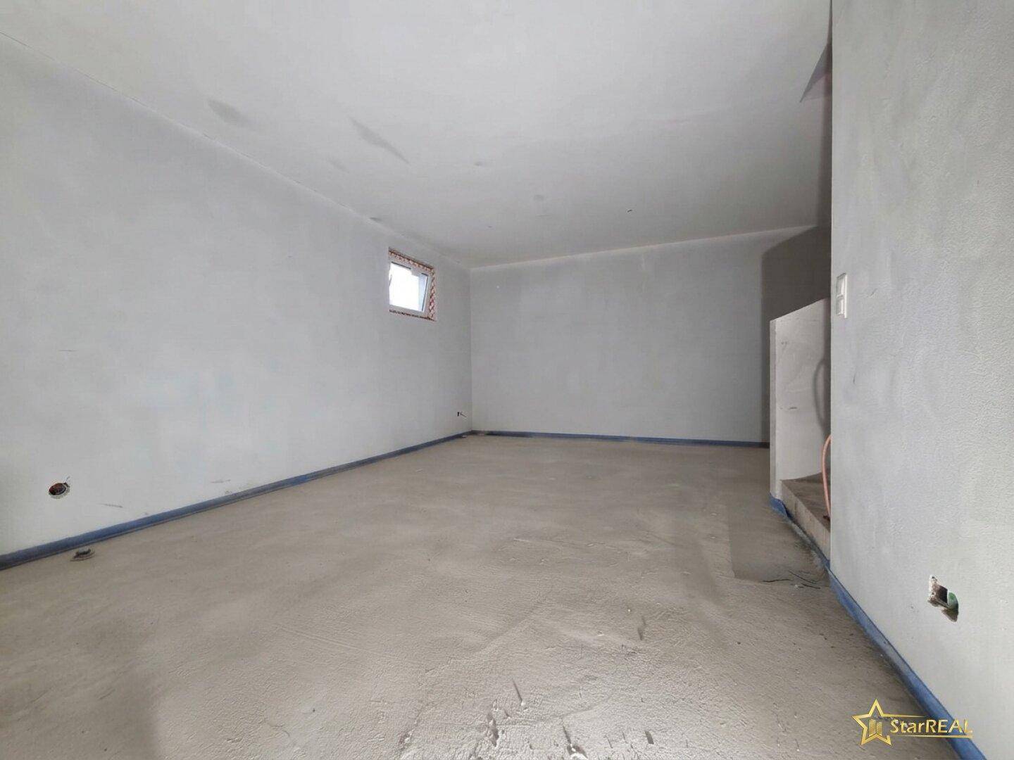 Zimmer im Rohbau mit kleinem Fenster und unfertigem Boden, bereit für den Ausbau.