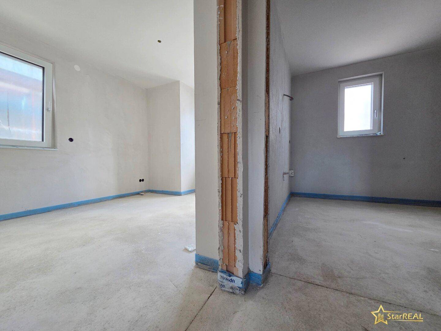 Zimmer im Rohbau mit Fenster und sichtbaren Ziegelwänden, bereit für den Innenausbau.