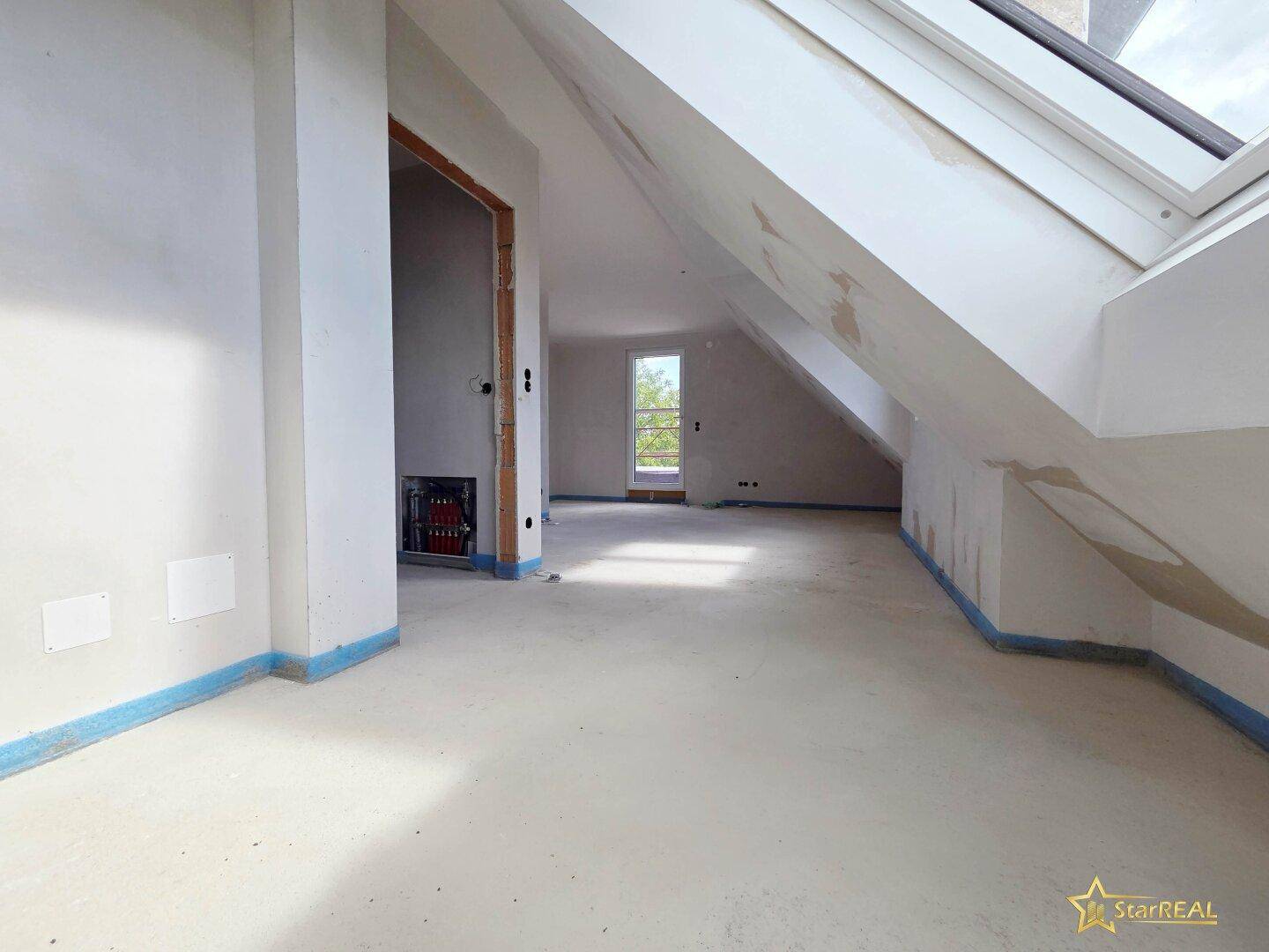 Helles Dachgeschoss im Rohbau mit Dachfenster und vorbereiteten Wänden für den Ausbau.
