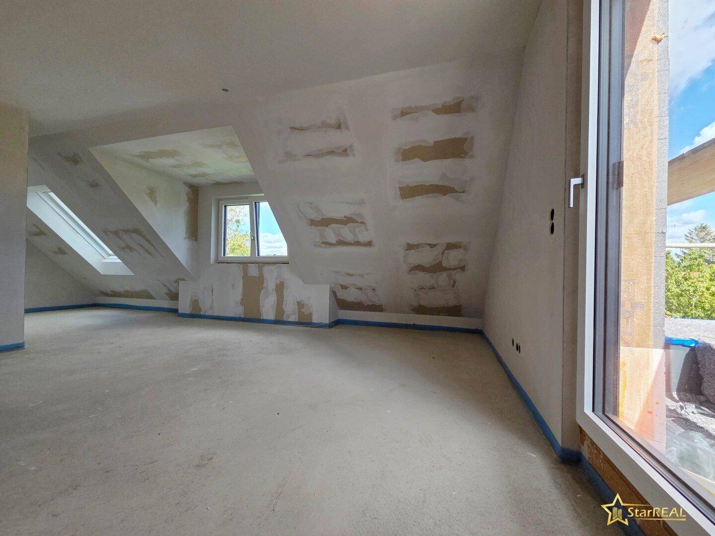 Helles Dachgeschosszimmer im Rohbau mit Dachfenstern und großem Fenster für viel Licht.