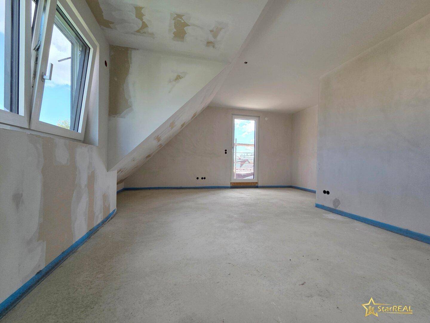 Unfertiges Zimmer im Dachgeschoss mit schräger Decke, Fenster und Zugang nach draußen.
