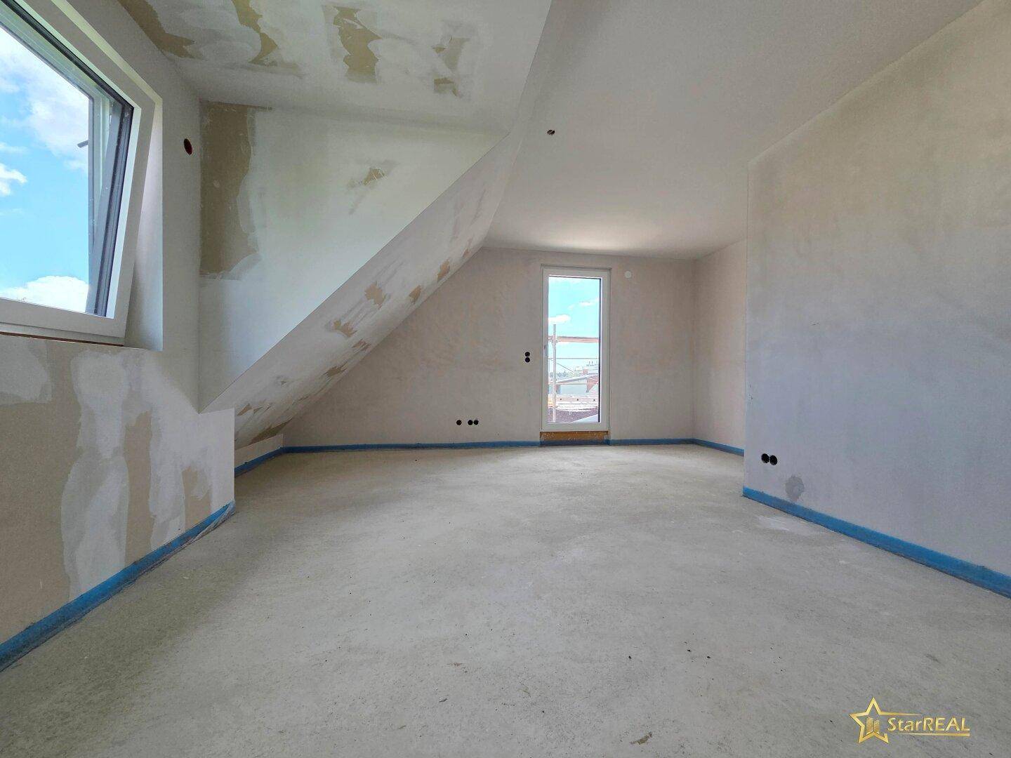 Unfertiges Zimmer im Dachgeschoss mit schräger Decke, Fenster und Zugang nach draußen.