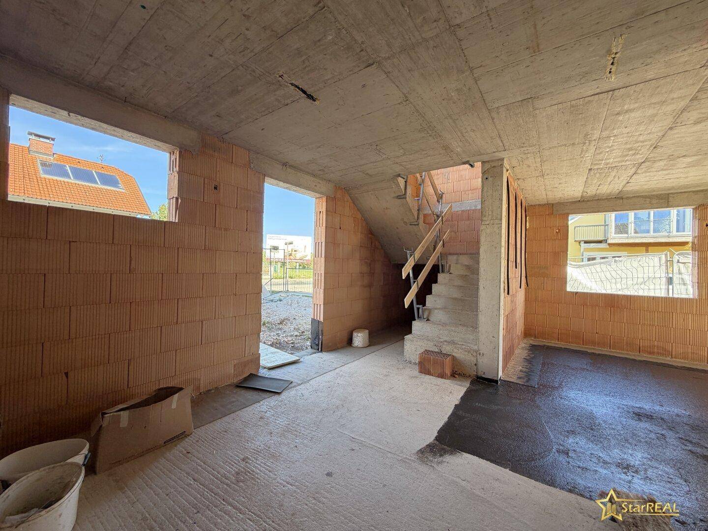 Eingangsbereich im Rohbau mit Treppenaufgang und Ziegelwänden, bereit für den Innenausbau.