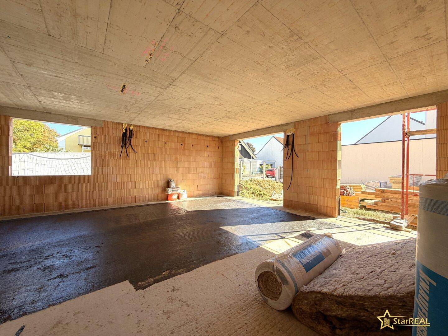 Innenraum im Rohbau mit Betonboden und Ziegelwänden, bereit für den weiteren Ausbau und viel Tageslicht.