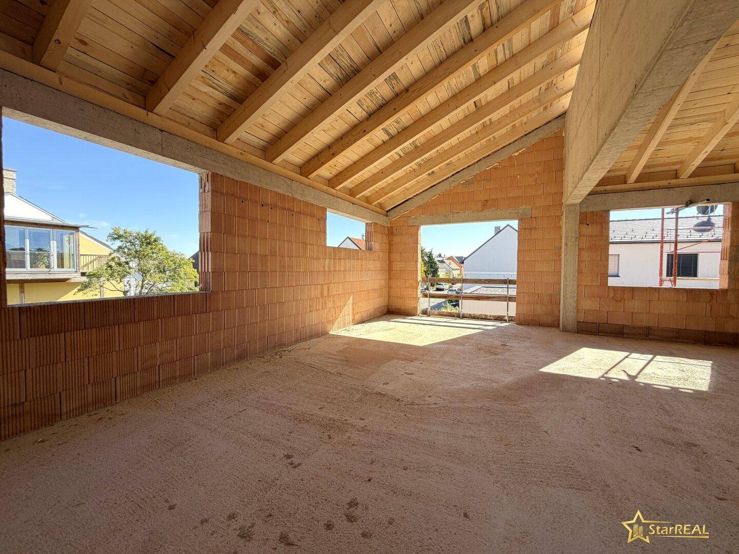 Dachgeschoss im Rohbau mit sichtbarer Holzkonstruktion und großen Fensteröffnungen für viel Licht.