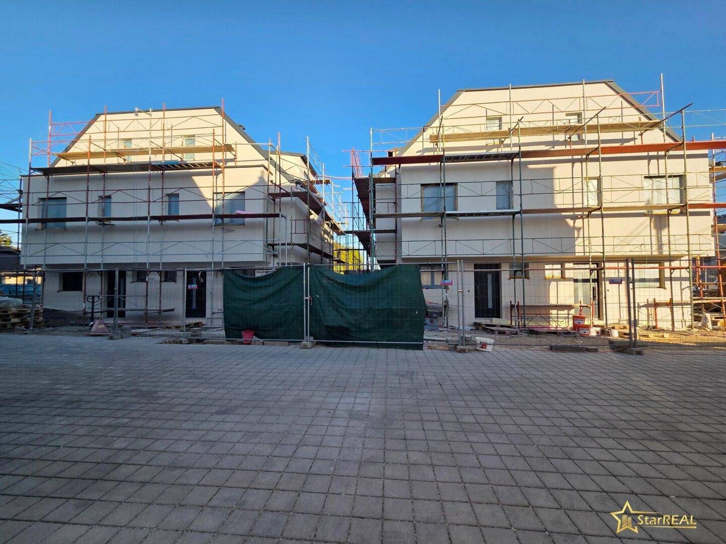 Zwei im Bau befindliche Reihenhäuser mit Gerüsten und Baustellenbereich davor.
