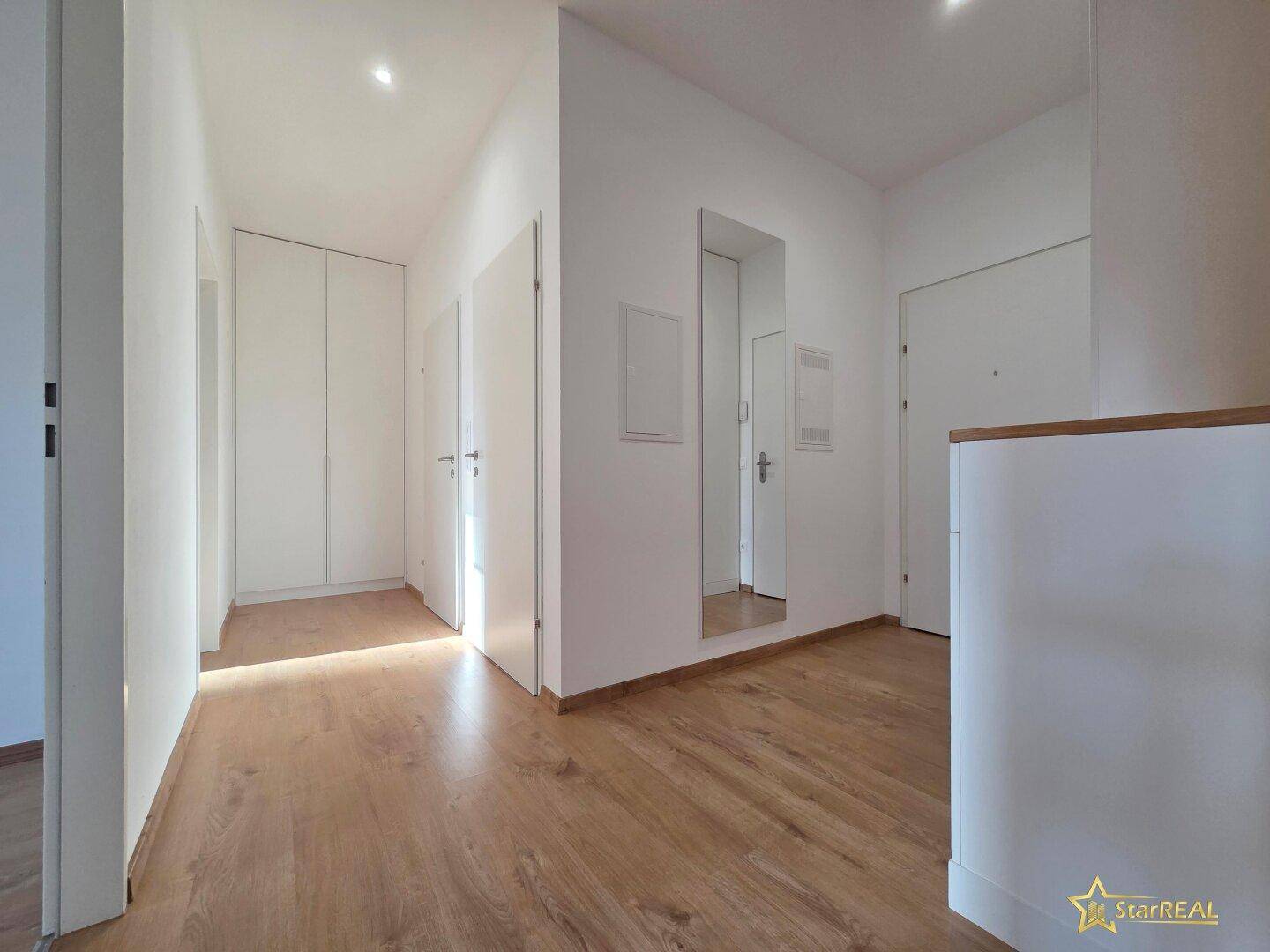 Heller Flur mit Laminatboden, weißen Wänden und integriertem Spiegel, der zu den Zimmern führt.