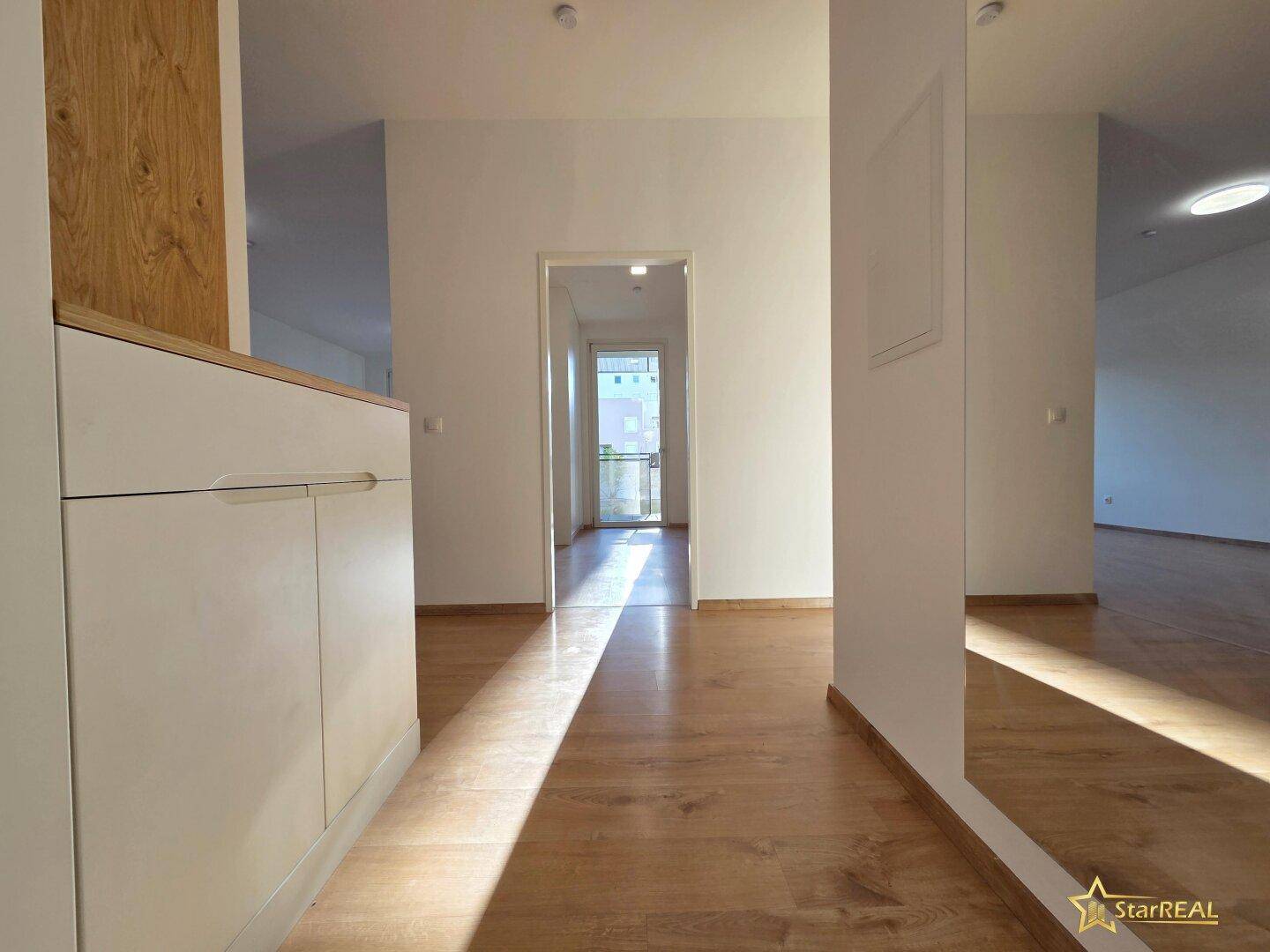 Lichtdurchfluteter Flur mit Laminatboden und weiß gestrichenen Wänden, der zu weiteren Räumen führt.