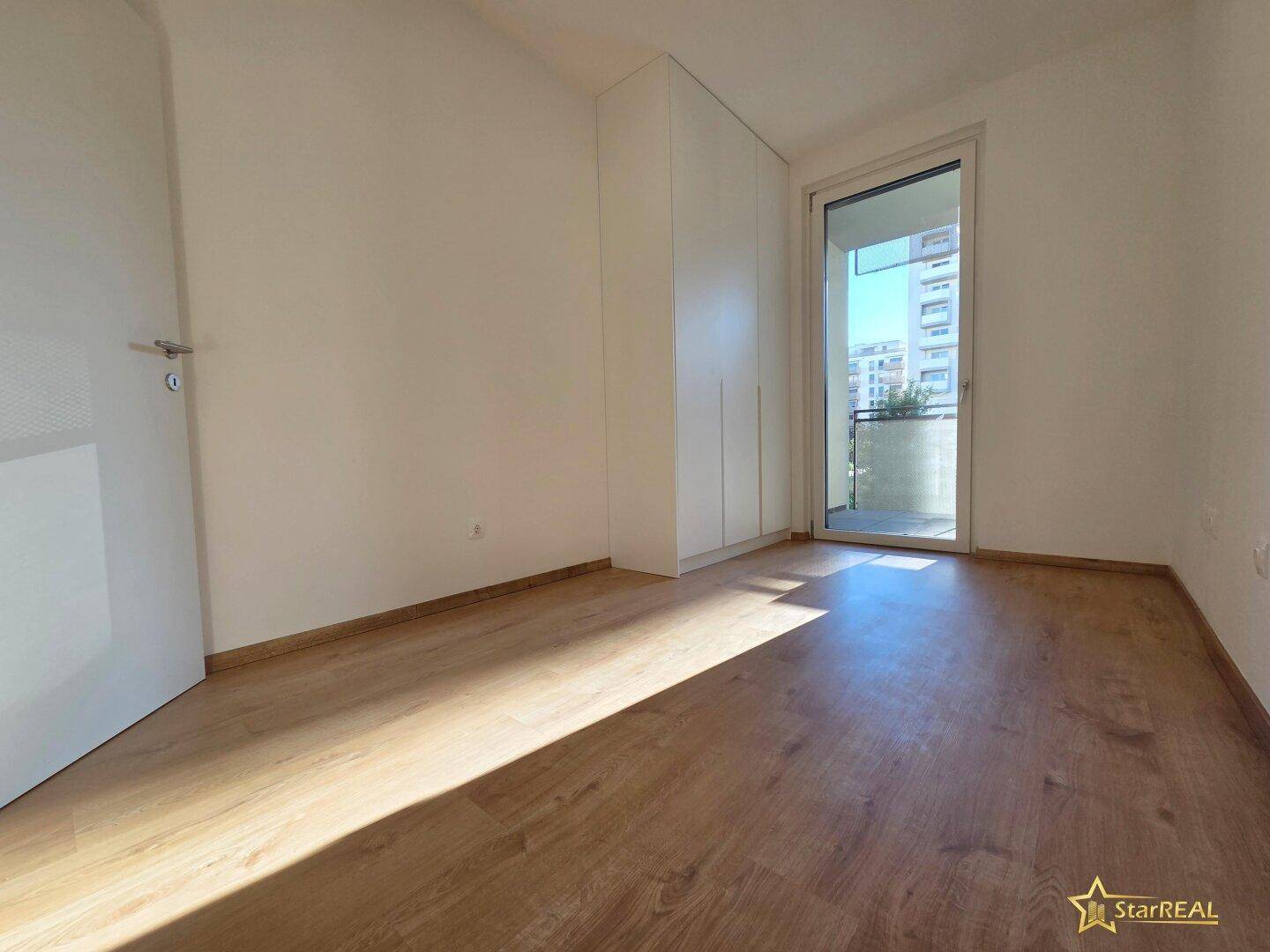 Helles Schlafzimmer mit Laminatboden, Einbauschränken und direktem Zugang zu einem Balkon.
