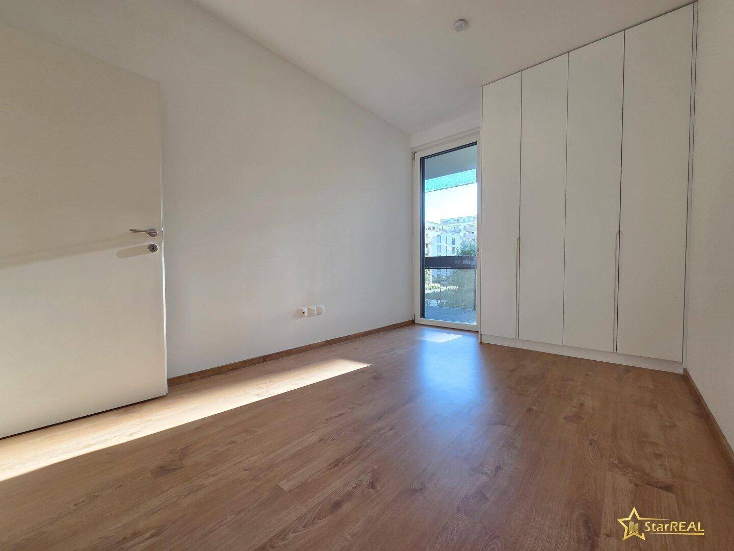 Geräumiges Schlafzimmer mit Laminatboden und großen Fenstern, die viel Tageslicht hereinlassen.