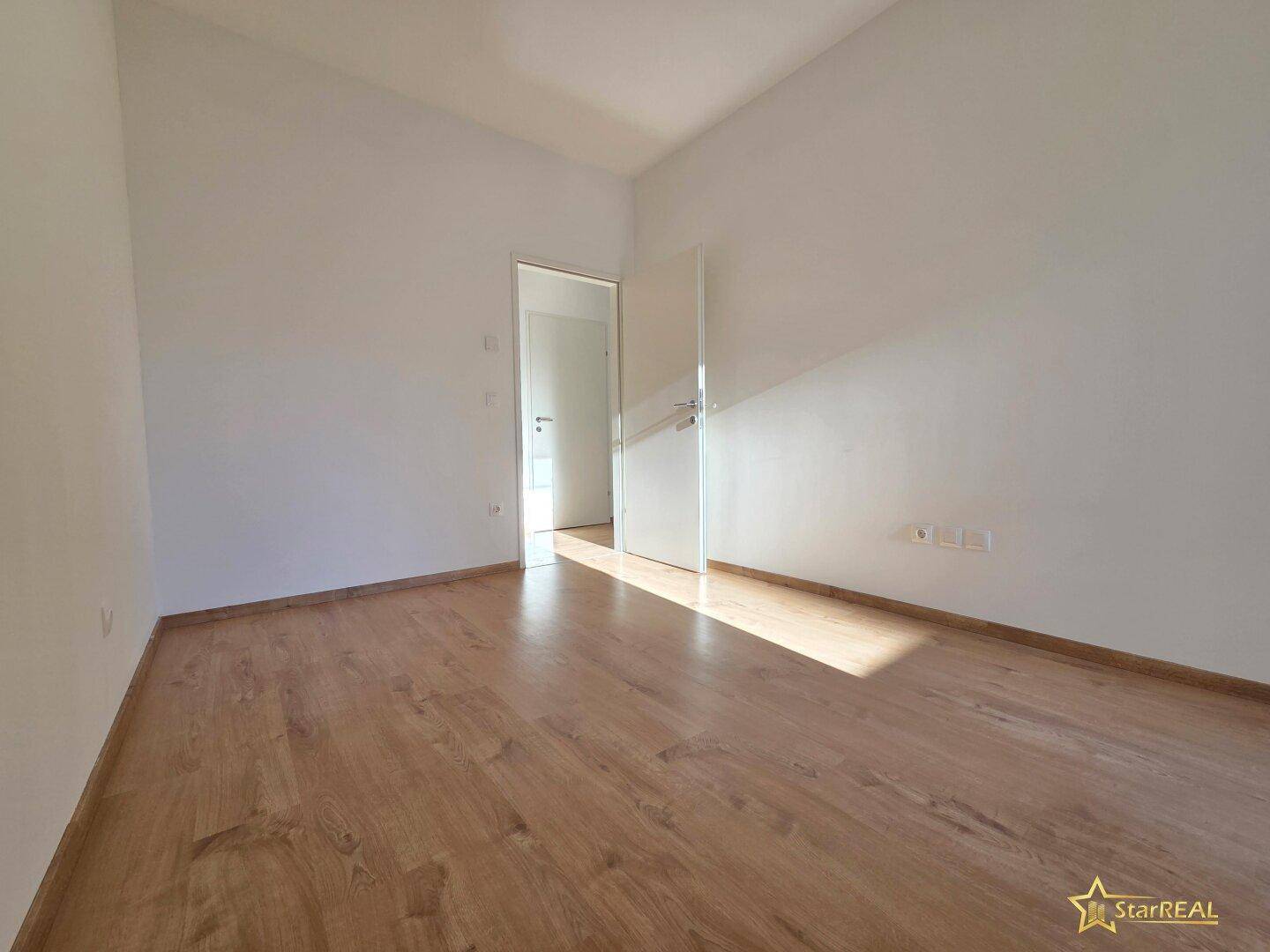 Leeres Zimmer mit Laminatboden und weißen Wänden, ideal als Schlafzimmer oder Arbeitszimmer nutzbar.