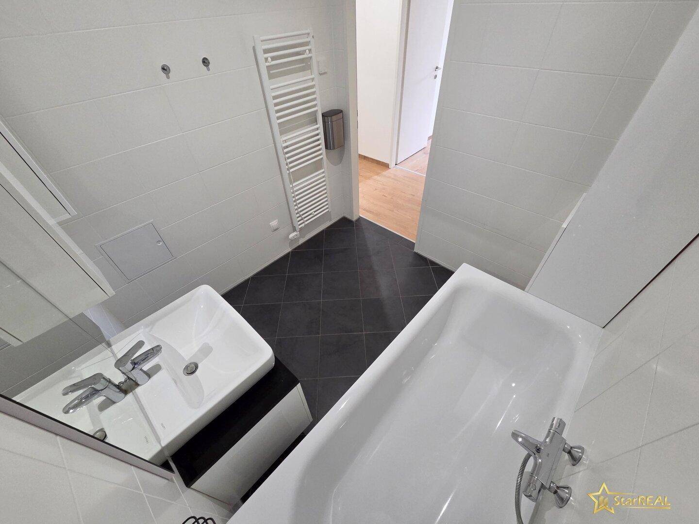 Modernes Badezimmer mit Badewanne, Einzelwaschbecken und dunklem Fliesenboden.