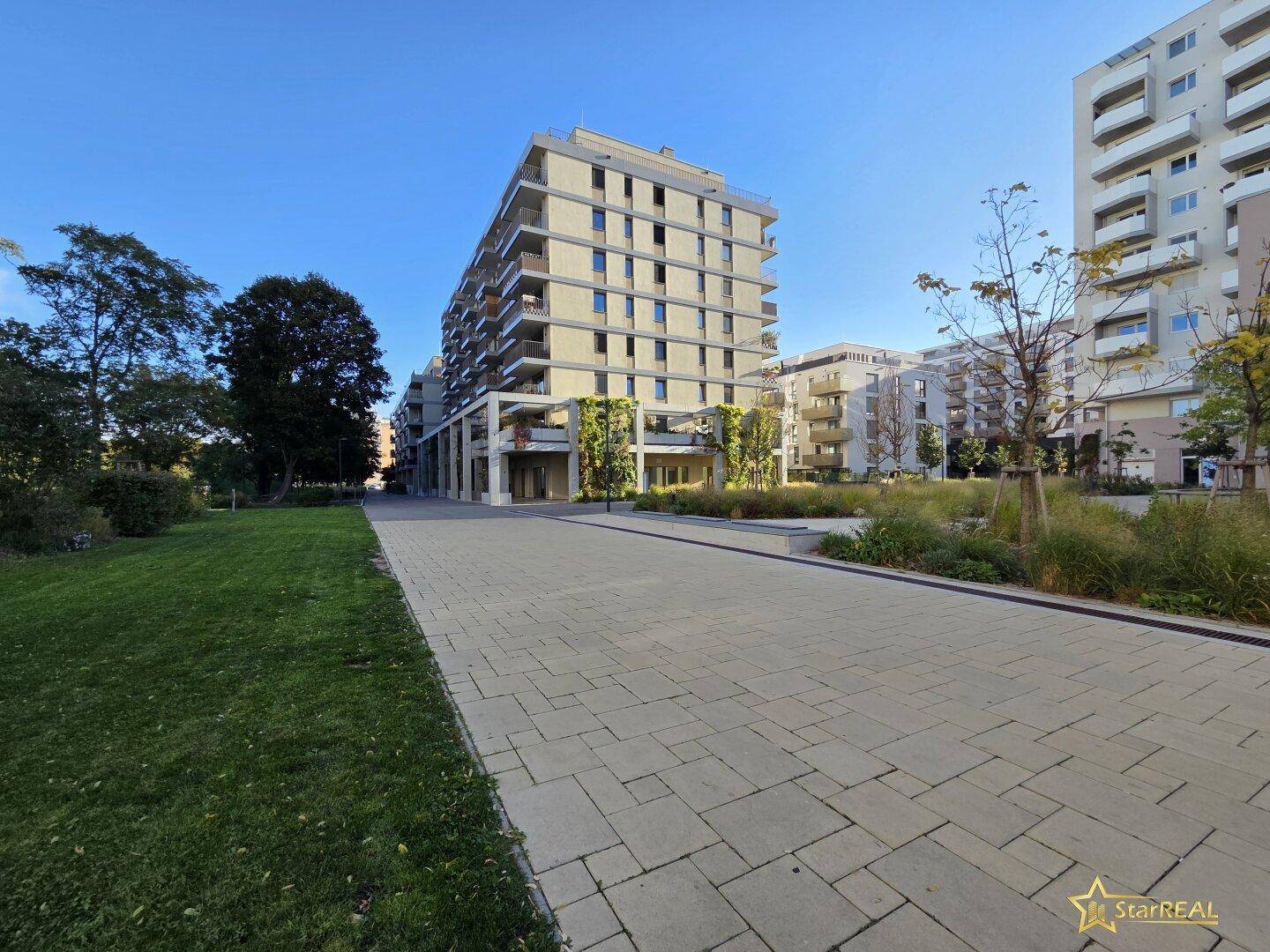 Modernes Wohngebäude mit Grünflächen und Gehwegen unter blauem Himmel.