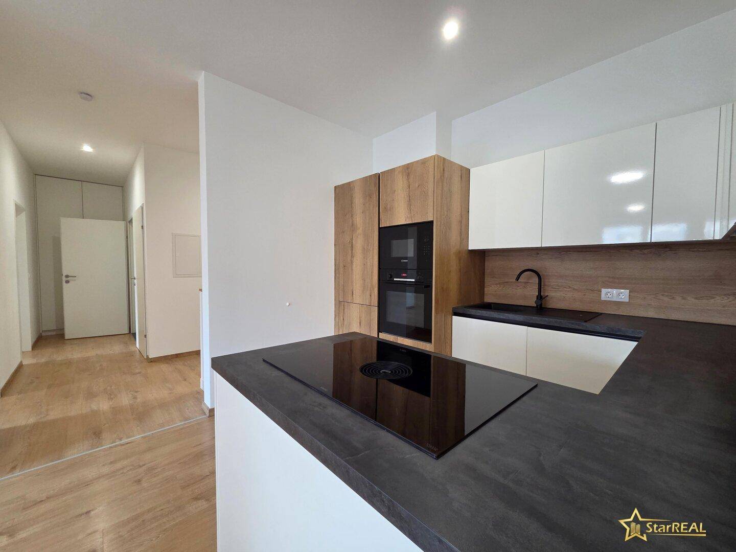 Offene, moderne Küche mit weißen Schränken, Holzdetails und Induktionskochfeld, angrenzend an den Flur.
