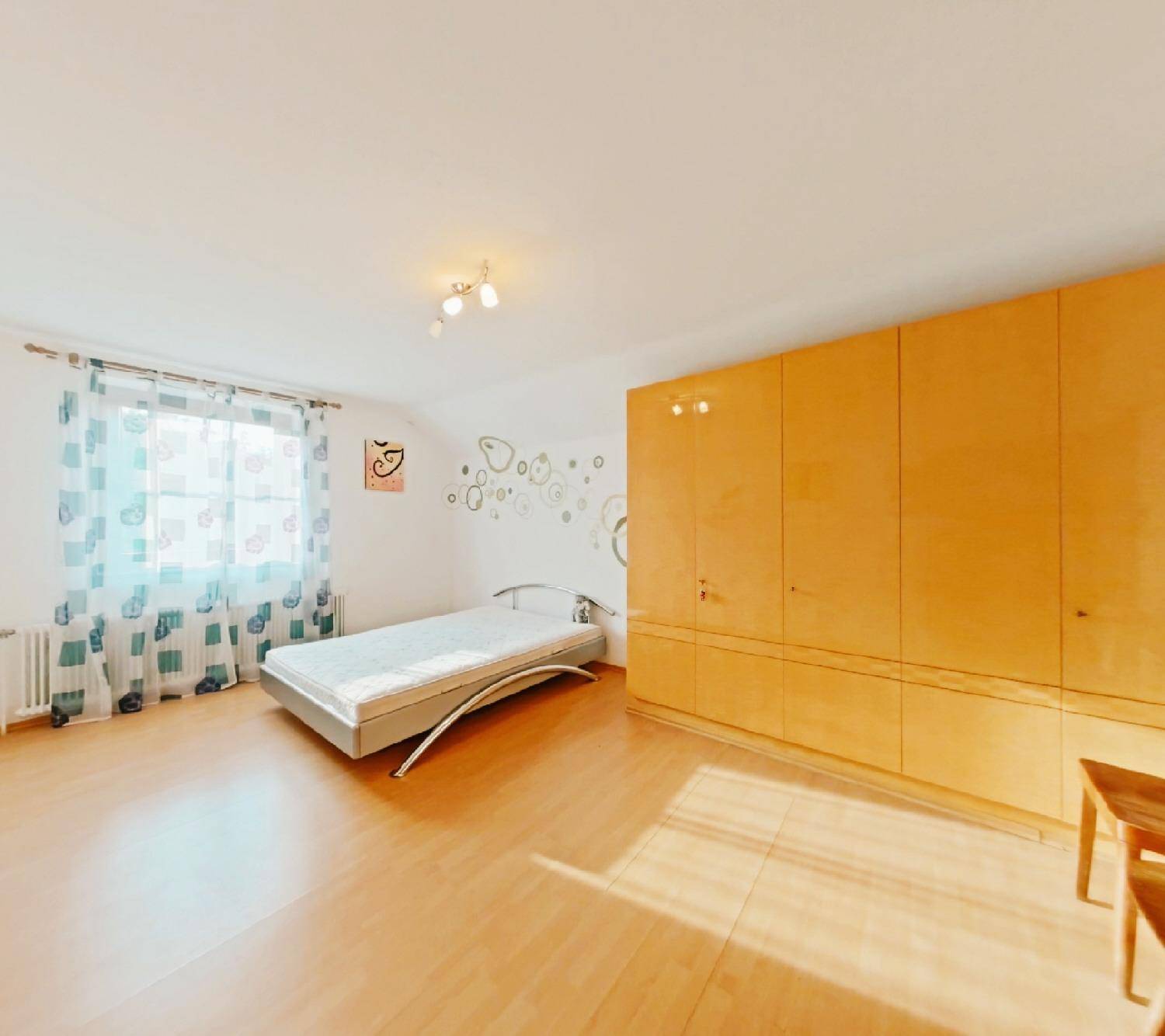 Schlafzimmer mit Einzelbett, Holzfußboden, großem Holzschrank und einem Fenster für natürliches Licht.