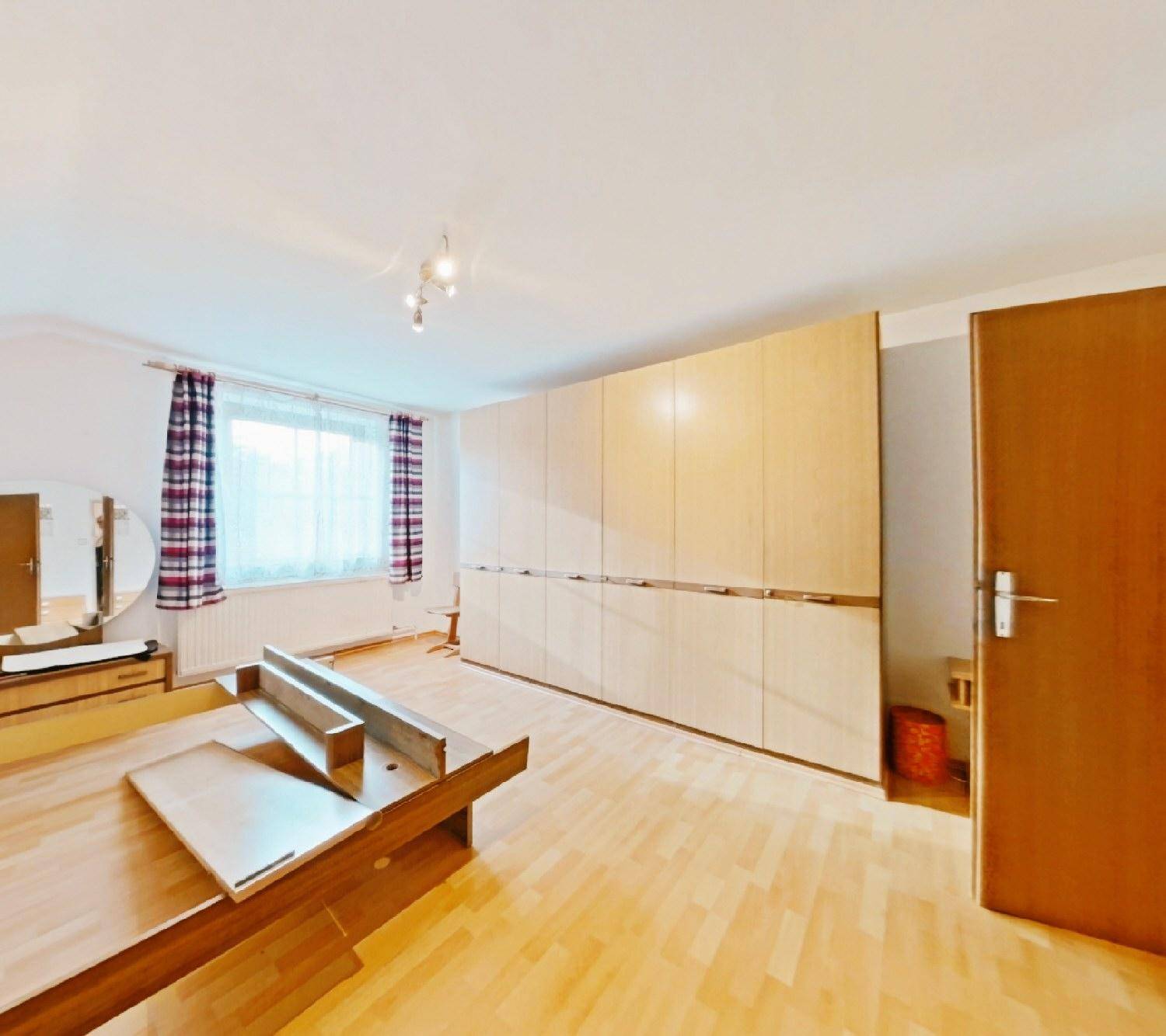 Schlafzimmer mit Holzfußboden, großem Kleiderschrank und einem Fenster, das den Raum erhellt.