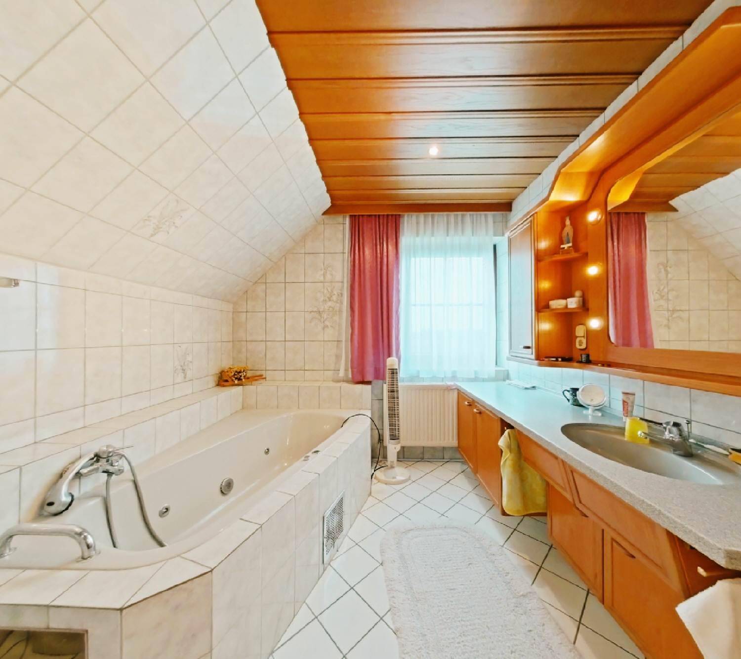 Helles Badezimmer mit Badewanne, Holzdecke und weißen Fliesen, ausgestattet mit einem Fenster.