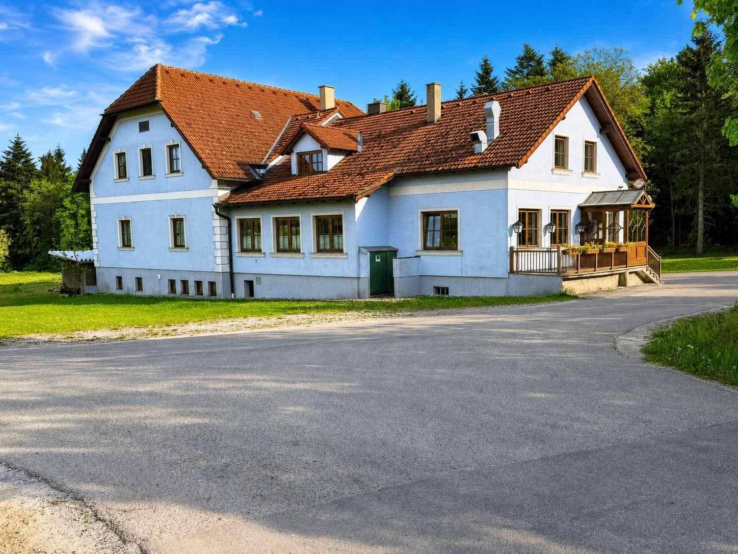 Ansprechendes Landhaus mit hellblauer Fassade und rotem Ziegeldach, umgeben von Natur.