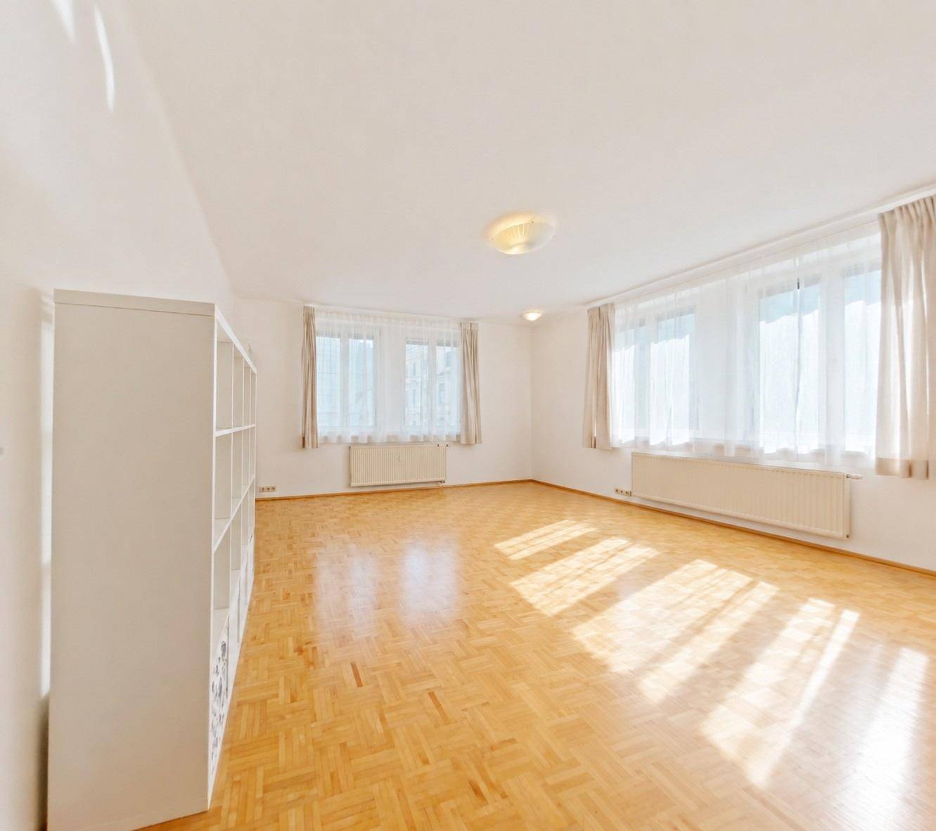 Heller, leerer Wohnraum mit Parkettboden, großen Fenstern und viel Tageslicht.