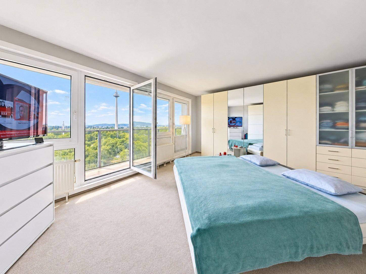 Helles Schlafzimmer mit Teppichboden, großen Einbauschränken und Zugang zum Balkon.