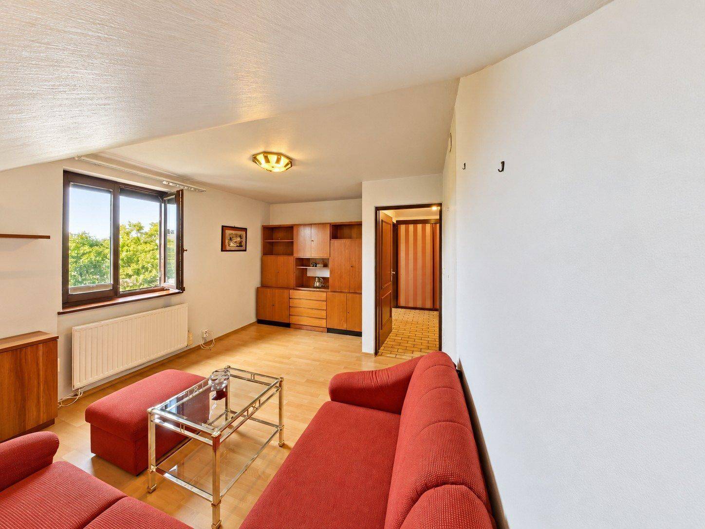 Gemütliches Wohnzimmer im Dachgeschoss mit rotem Sofa und Blick ins Grüne.