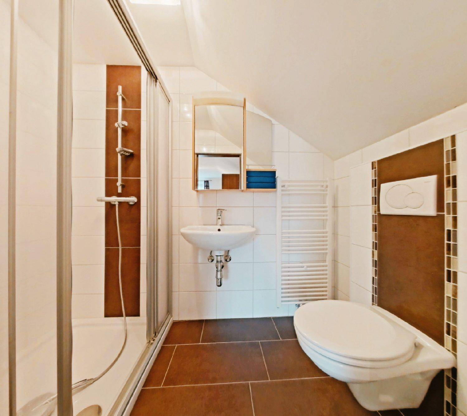 Badezimmer mit Duschkabine, braunen und weißen Fliesen, Wand-WC und Dachschräge.