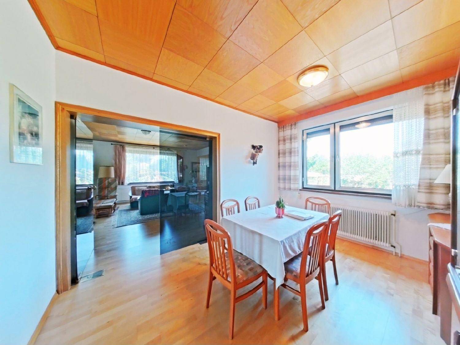Essbereich mit Holztisch und Stühlen, Parkettboden und Blick in das angrenzende Wohnzimmer.