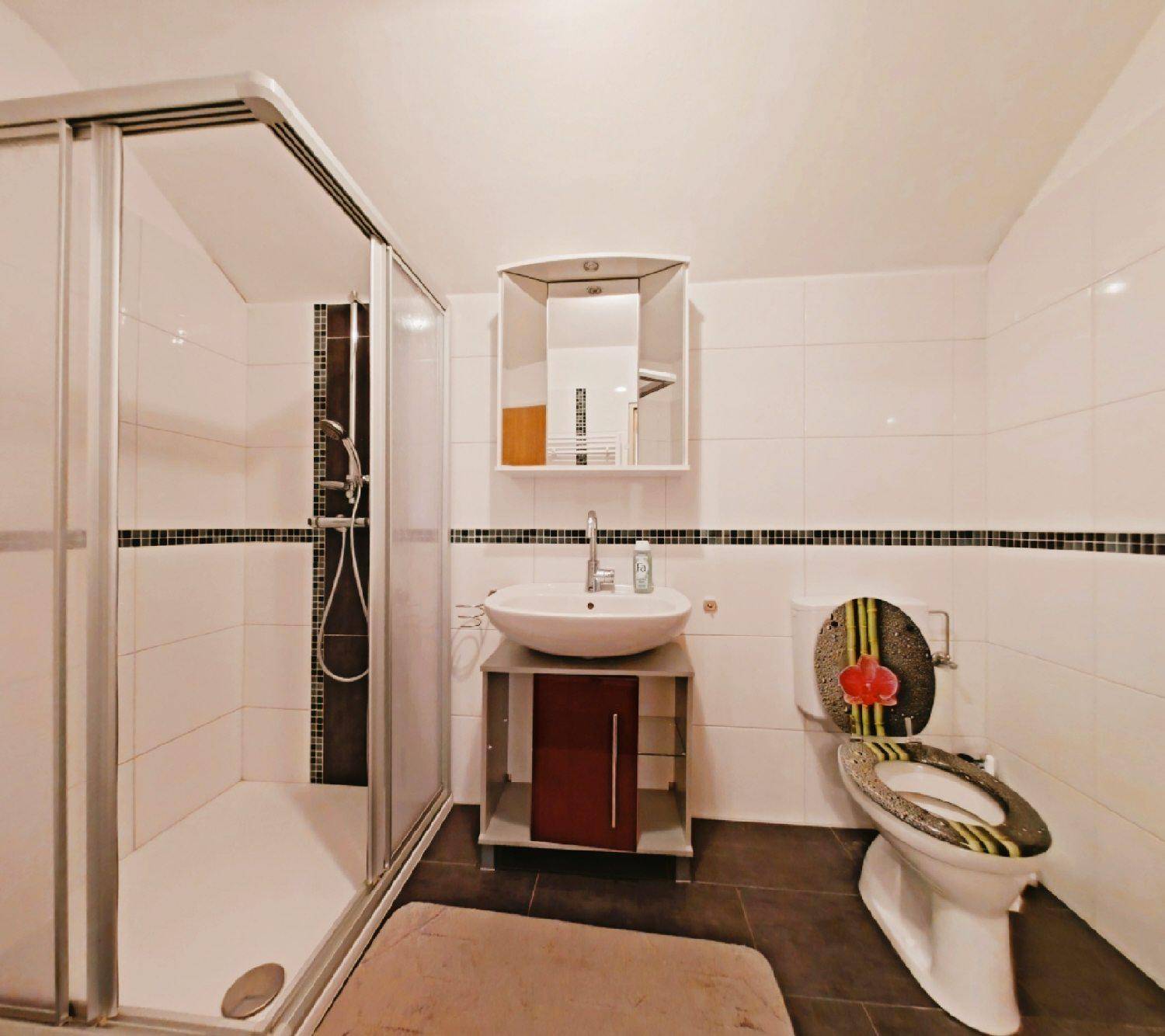 Modernes Badezimmer mit Duschkabine, weißen und dunklen Fliesen sowie einem Waschbecken mit Unterschrank.