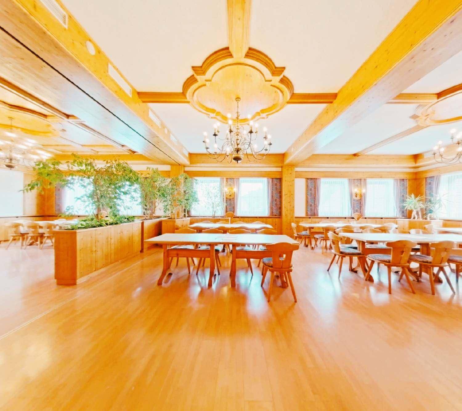 Großer Speisesaal mit Holztischen, Stühlen, Holzbalkendecke und eleganten Kronleuchtern.