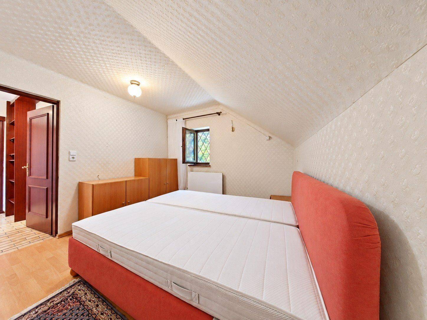 Schlafzimmer im Dachgeschoss mit Doppelbett, Holzmöbeln und schrägen Wänden.