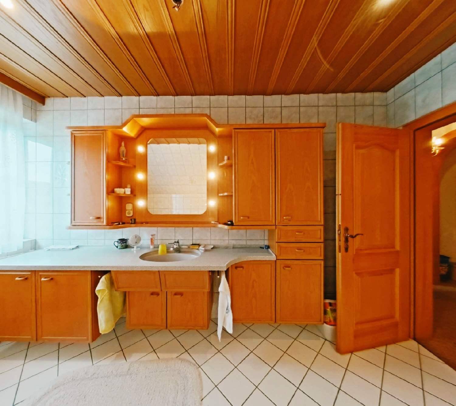 Badezimmer mit Holzdecke, weißen Fliesen und einem großen Holzwaschtisch mit beleuchtetem Spiegel.