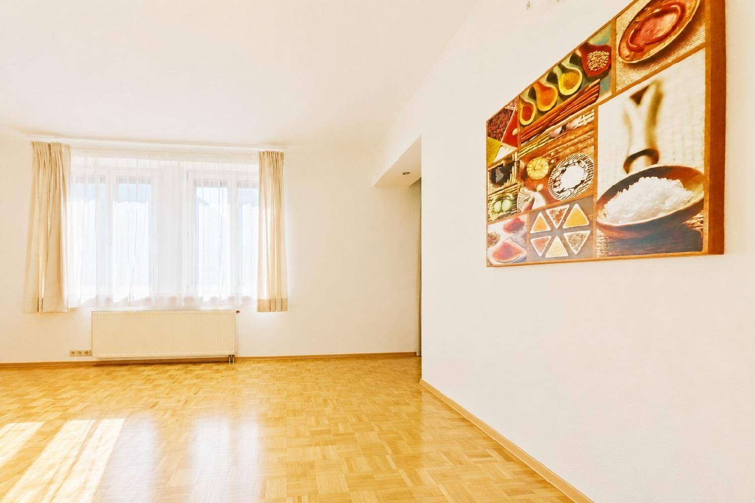 Geräumiger Wohnbereich mit Parkettboden, hellem Fenster und dekorativem Wandbild.