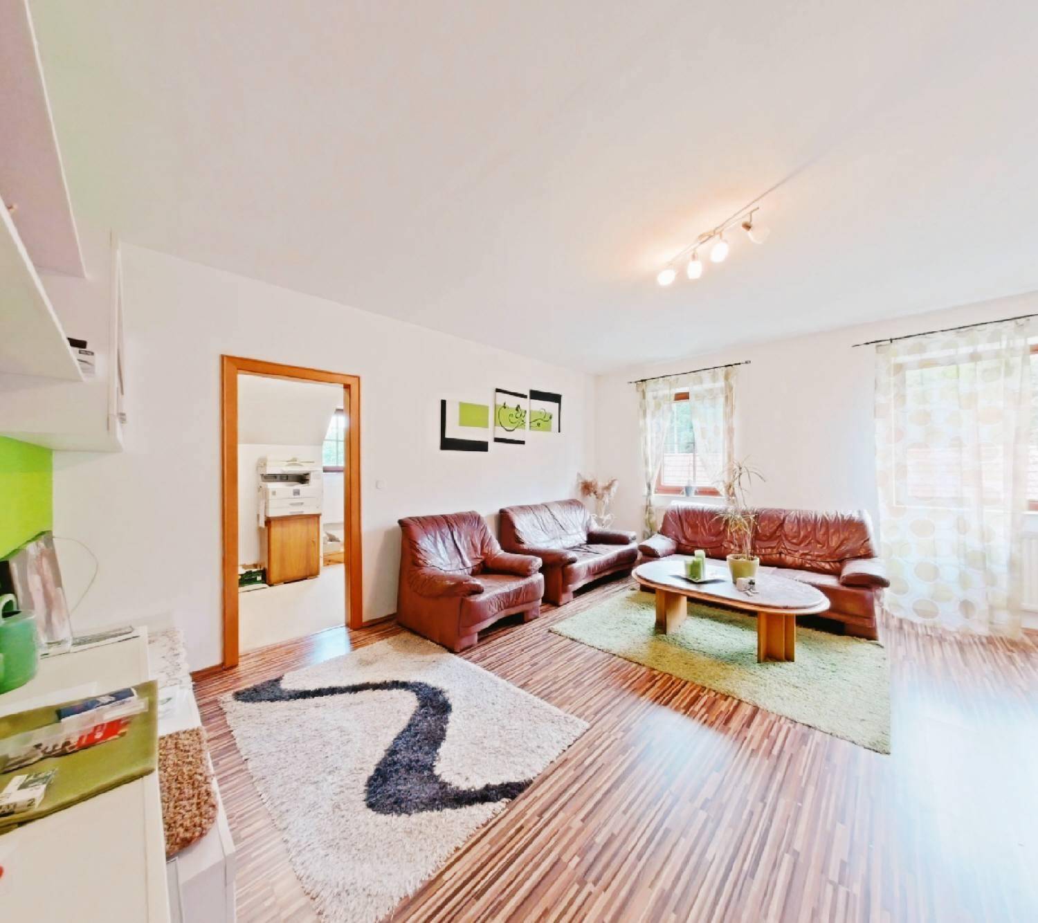 Gemütliches Wohnzimmer mit braunen Ledersofas, Laminatboden und einem grünen Teppich.