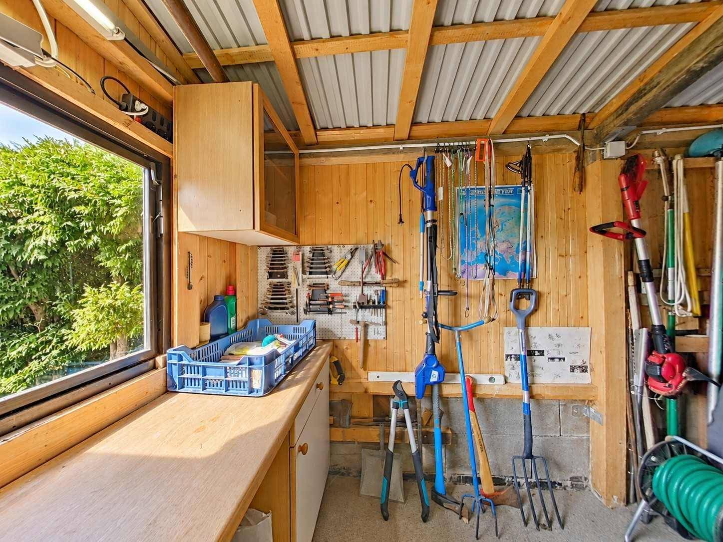 Geräteschuppen mit Werkbank, Holzverkleidung und verschiedenen Gartenwerkzeugen.