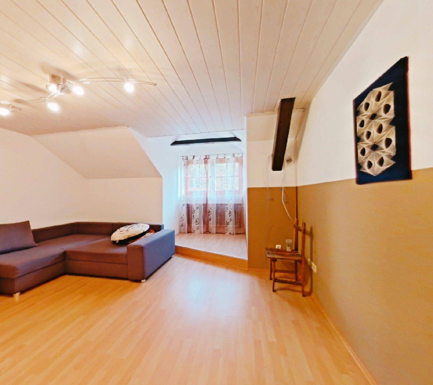 Wohnbereich mit Ecksofa, Holzfußboden und einer Holzpaneeldecke unter der Dachschräge.
