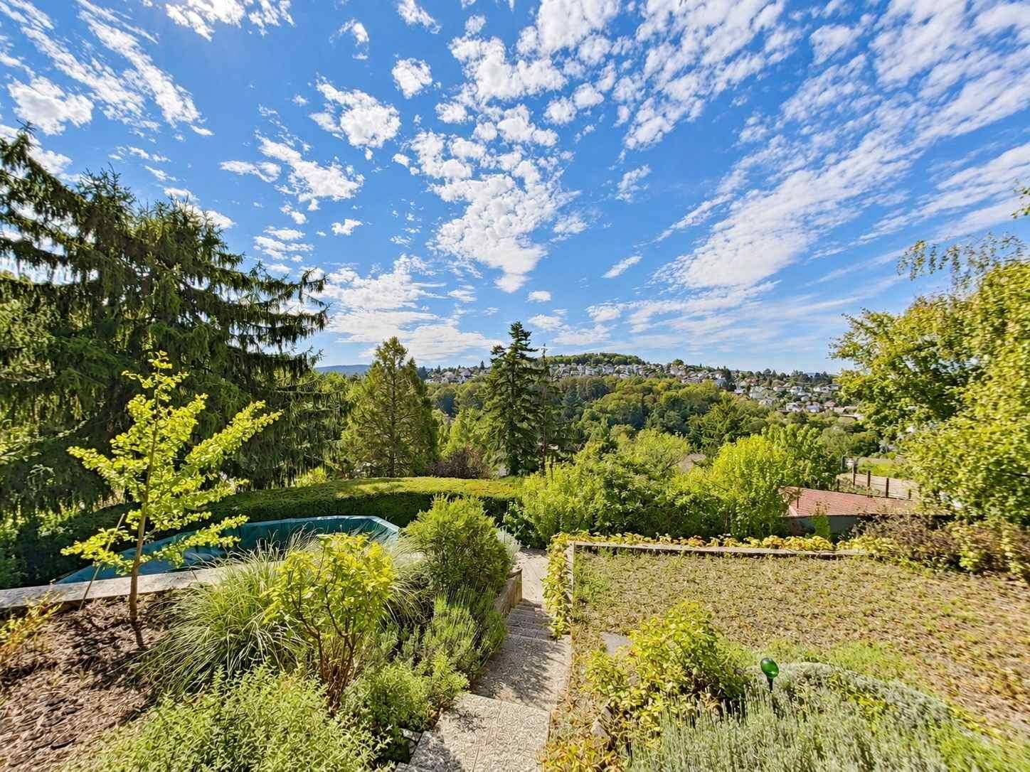 Weitläufiger Garten mit vielfältiger Bepflanzung, Stufen und Panoramablick in die Landschaft.