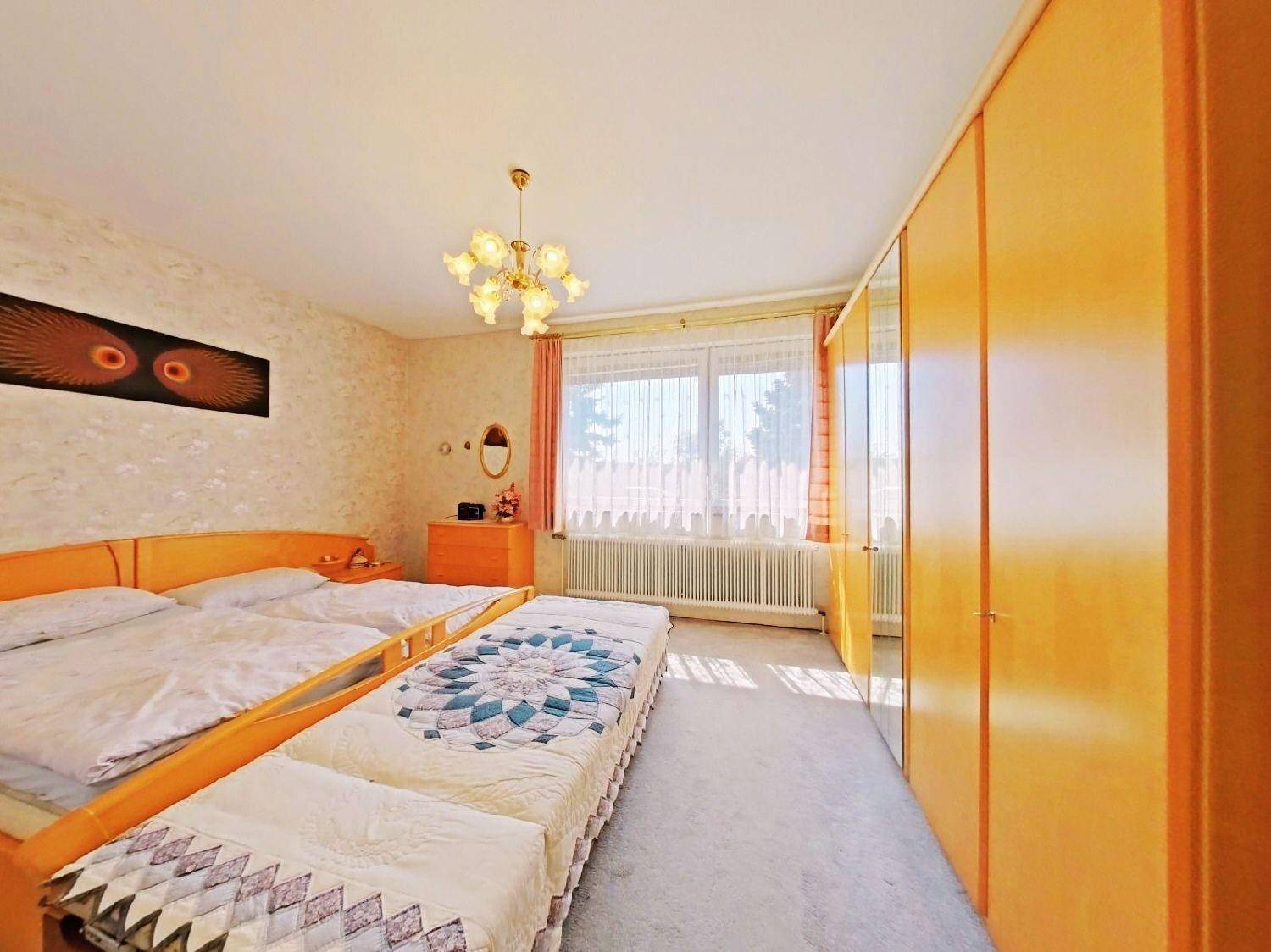 Helles Schlafzimmer mit Doppelbett, Teppichboden und großen Fenstern.