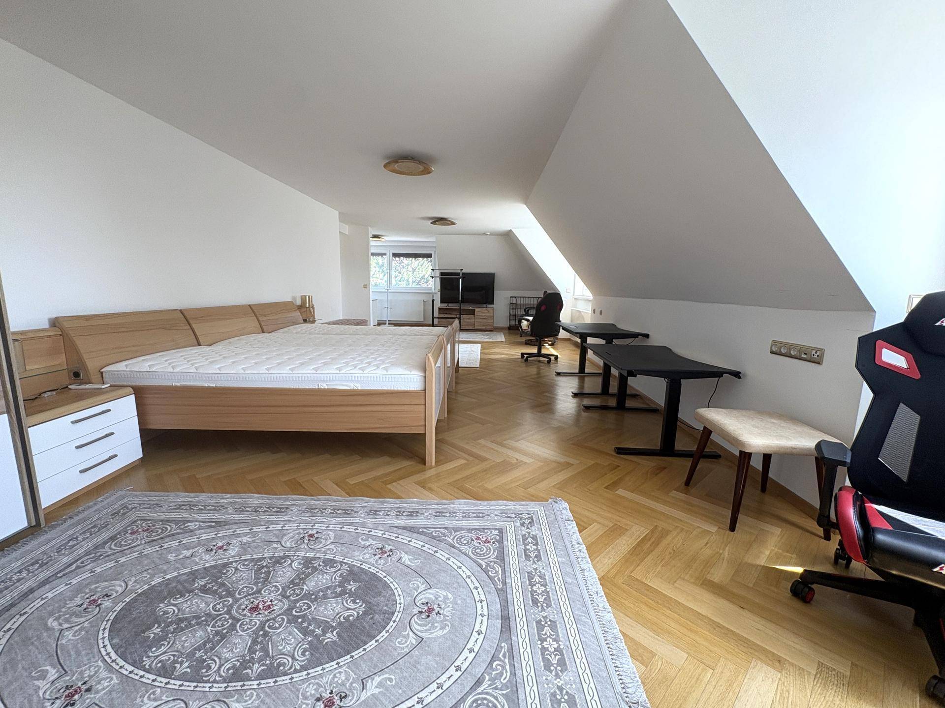 Helles Dachgeschosszimmer mit Holzbett, Schreibtischen und Fischgrätparkett, bietet viel Platz und Tageslicht.