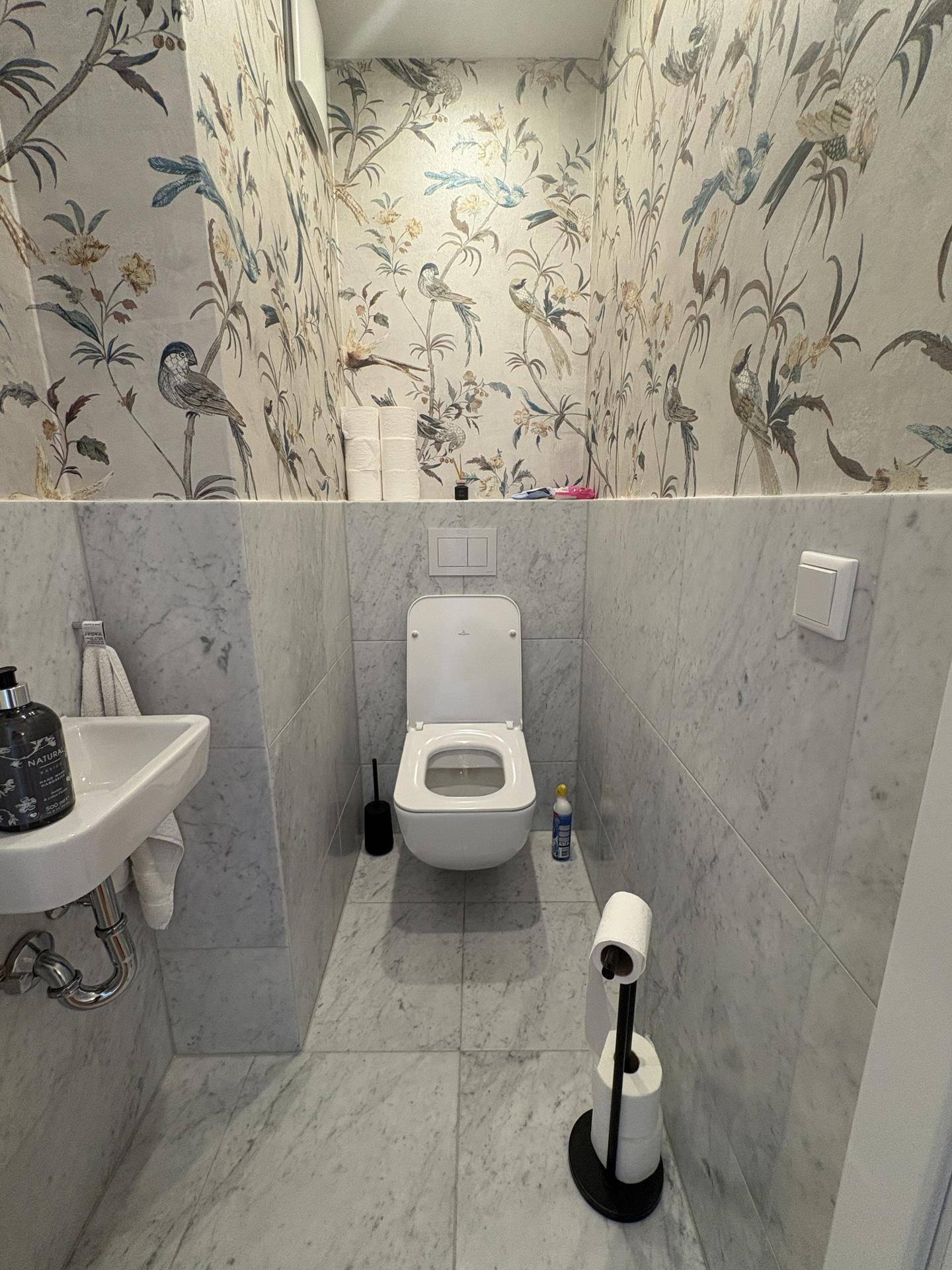 Kleines Gäste-WC mit floraler Tapete, Marmorfliesen und modernem Wand-WC.
