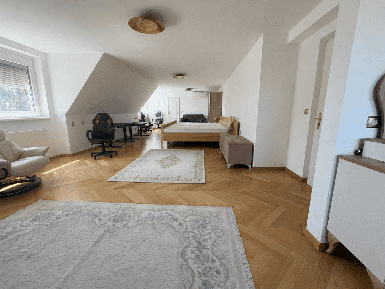 Geräumiges Dachgeschosszimmer mit Bett, Schreibtisch und Sitzgelegenheiten, ideal als Schlaf- oder Arbeitsbereich.
