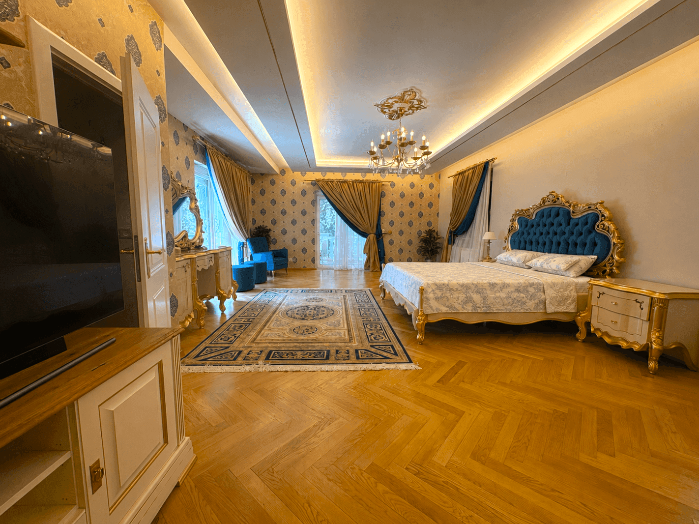 Geräumiges Schlafzimmer mit luxuriöser Einrichtung, Fernseher und Zugang zu einem Außenbereich, betont durch elegantes Parkett.