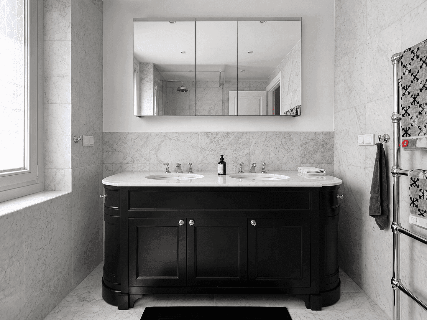 Luxuriöses Badezimmer mit schwarzem Doppelwaschtisch, Marmoroberflächen und Spiegelschrank.