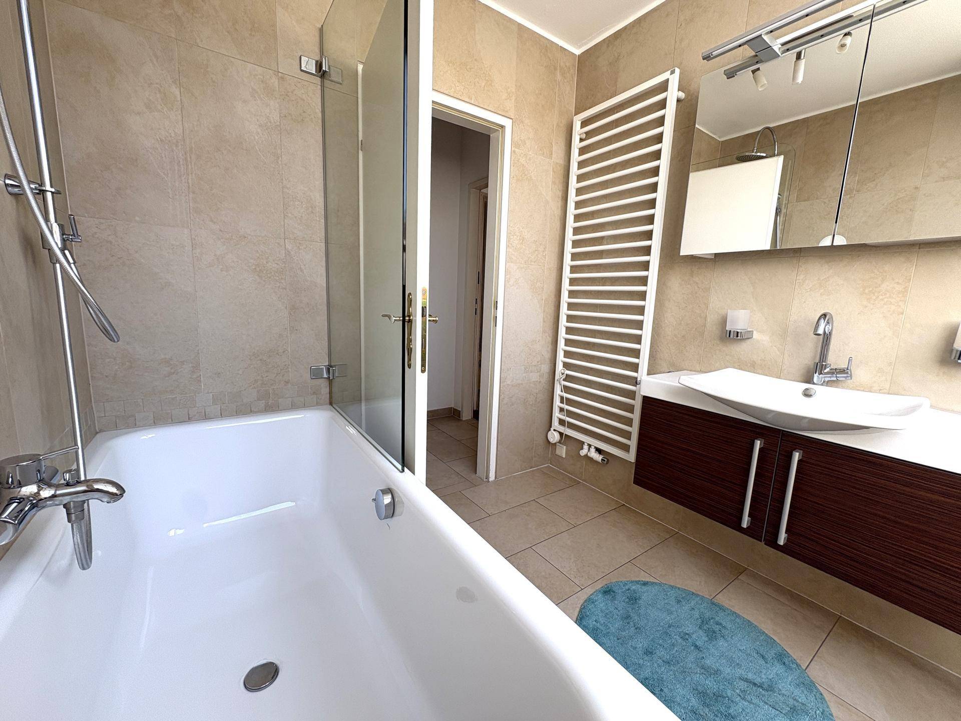 Helles Badezimmer mit Badewanne, Duschfunktion und modernem Waschtisch, ausgestattet mit Handtuchheizkörper.