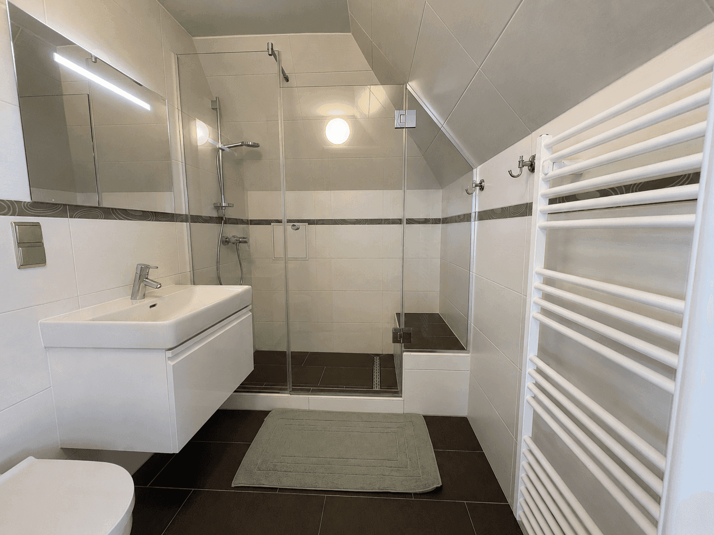 Modernes Badezimmer mit begehbarer Dusche, Waschtisch und beheiztem Handtuchhalter unter Dachschräge.