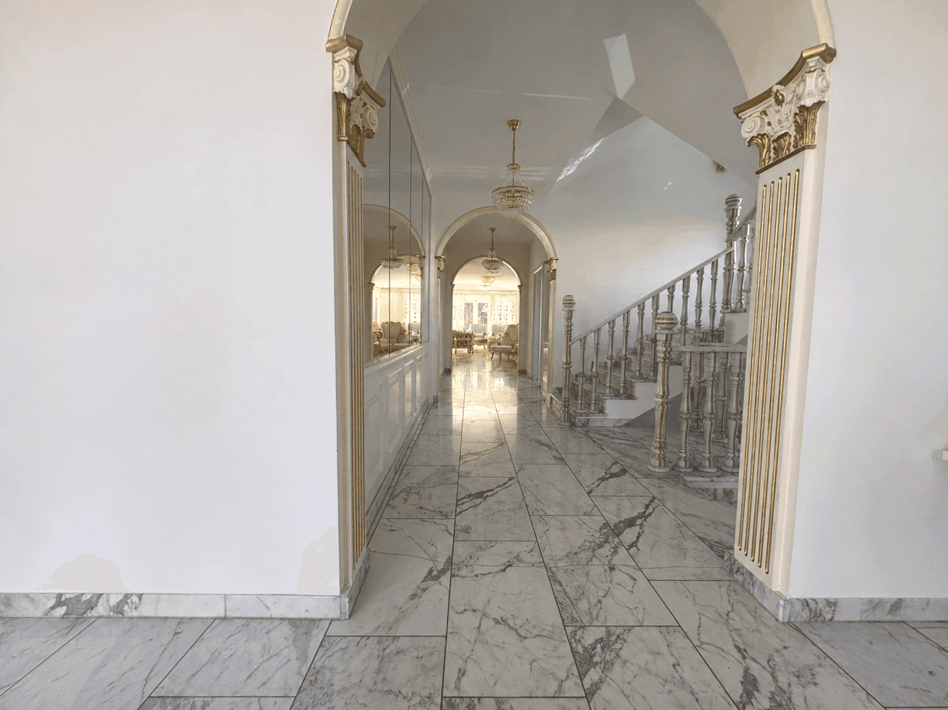 Langer, eleganter Flur mit Marmorboden, goldenen Akzenten und Blick auf die Treppe.
