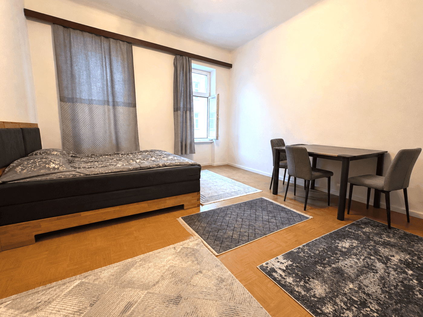 Geräumiges Schlafzimmer mit Holzbett, Esstisch und Fenster, das viel Tageslicht hereinlässt.