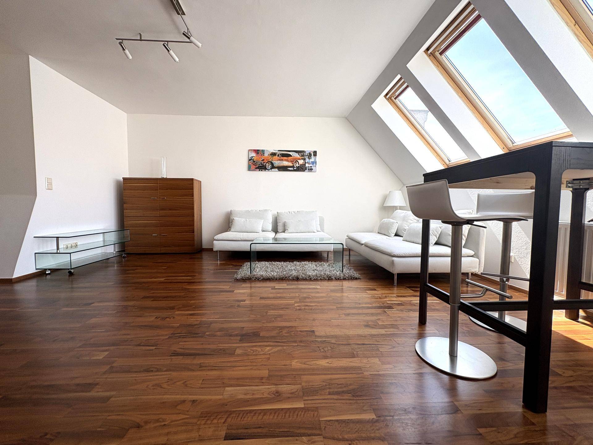 Geräumiger Wohnbereich mit dunklem Holzboden, bequemen Sofas und großen Dachfenstern für viel Tageslicht.